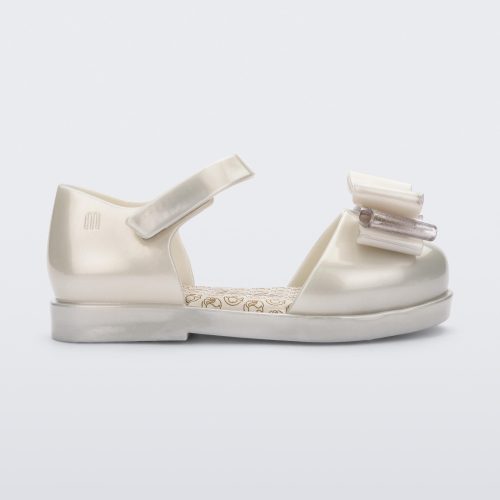 Side view of a white metallic Mini Melissa sandal with a Barbie bow detail on the front toe, white metallic ankle strap and a Barbie logo sole