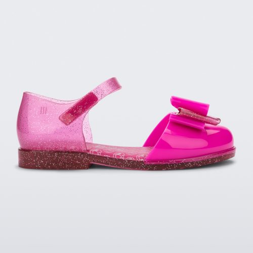 Side view of a glitter pink Mini Melissa sandal with a Barbie bow detail on the front toe, pink glitter ankle strap and a Barbie logo sole