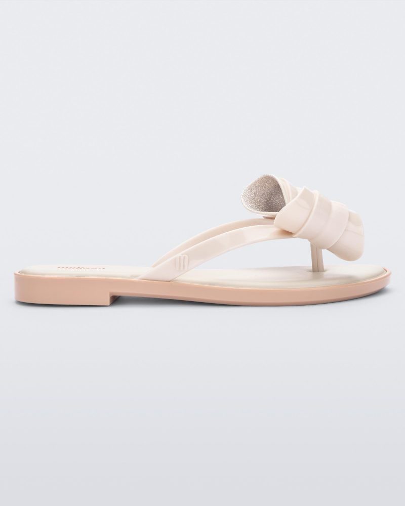 Side view of a Melissa slim strap flip flop in light beige with bow applique