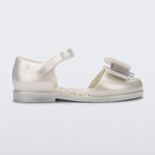 Side view of a metallic white Mini Melissa sandal with a Barbie bow detail on the front toe, metallic white ankle strap and a Barbie logo sole