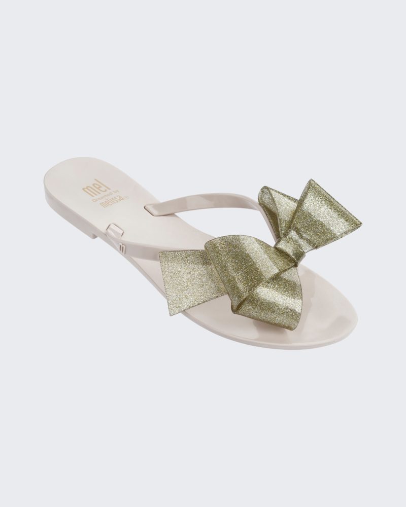 An angled top view of a White/Gold Glitter Mini Melissa Harmonic Bow flip flop with a white sole, straps and gold glitter bow.