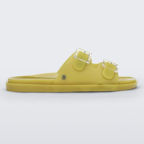 Side view of a yellow Melissa Wide Slide with two straps fastened on top with two clear buckles and a "m" logo on the side.