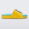 Side view of a pair of yellow Mini Melissa Cloud slide with a blue insole, yellow base and a cartoon drawn smiley face on the front.