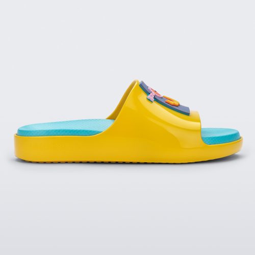 Side view of a pair of yellow Mini Melissa Cloud slide with a blue insole, yellow base and a cartoon drawn smiley face on the front.