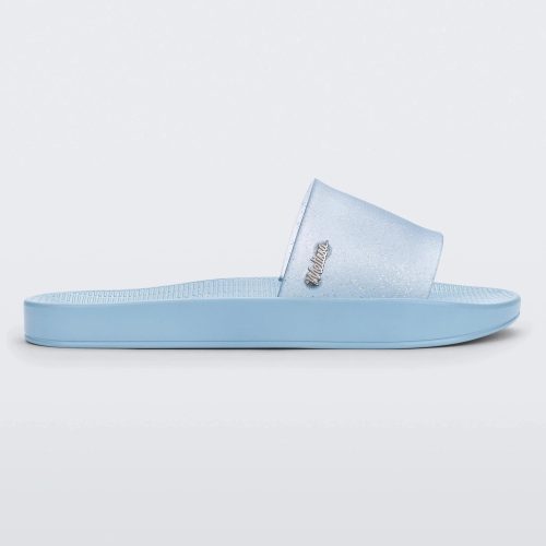 Side view of a blue/clear glitter Melissa Sun Sunset slide with a blue sole and clear blue glitter front strap.