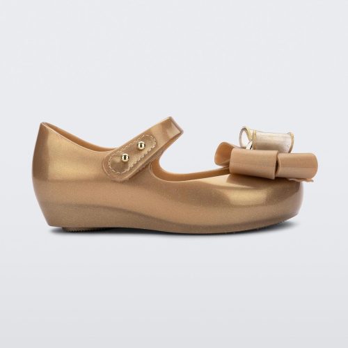 Side view of a gold Mini Melissa Ultragirl Sweet flat with a top strap and a bow detail on the toe.