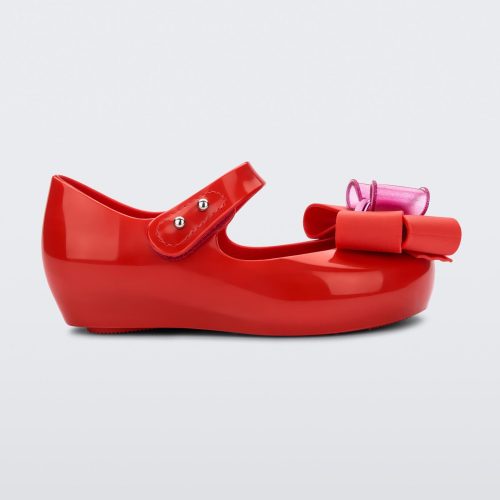 Side view of a red Mini Melissa Ultragirl Sweet flat with a top strap and a pink and red bow detail on the toe.