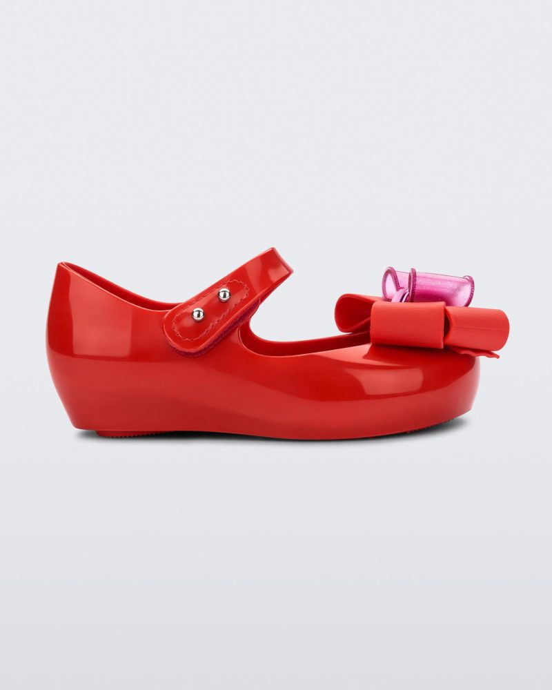 Side view of a red Mini Melissa Ultragirl Sweet flat with a top strap and a pink and red bow detail on the toe.