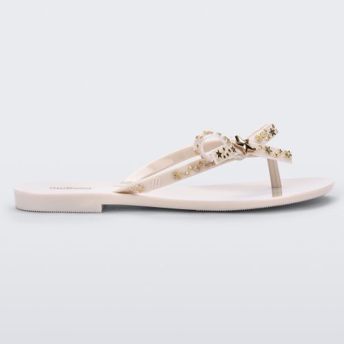 Side view of a beige Melissa Harmonic Stars flip flop with a bow and gold star details on the straps.