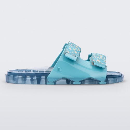 Side view of a blue multicolor Melissa Brave Wide Slide with a blue base, blue and green floral print velcro straps and a translucent blue insole.