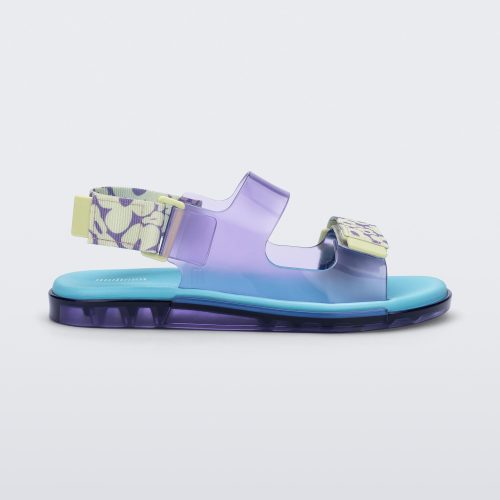 Side view of a lilac Melissa Brave Papete sandals with a blue insole, purple and green flower print and transparent lilac straps and a velcro back.