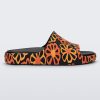 Side view of a multicolor matte mosaic flower Melissa Cloud slide with a black base and an orange and yellow flower pattern, with a black insole reading in orange "Melissa Miller" and "Melissa Simon" on different shoes