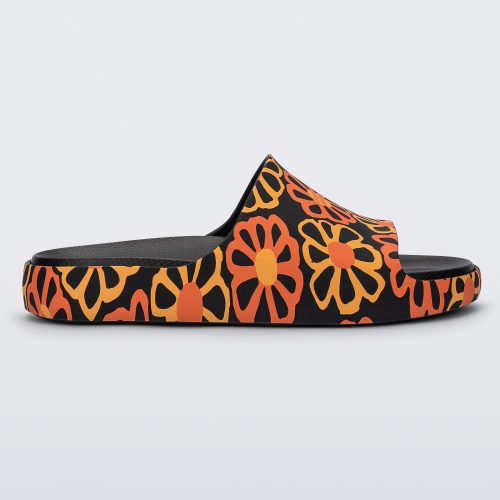 Side view of a multicolor matte mosaic flower Melissa Cloud slide with a black base and an orange and yellow flower pattern, with a black insole reading in orange 