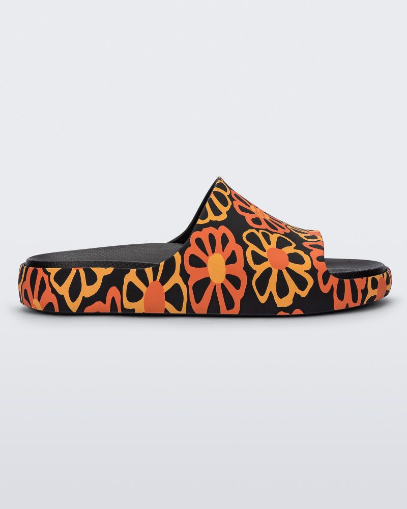 Side view of a multicolor matte mosaic flower Melissa Cloud slide with a black base and an orange and yellow flower pattern, with a black insole reading in orange "Melissa Miller" and "Melissa Simon" on different shoes