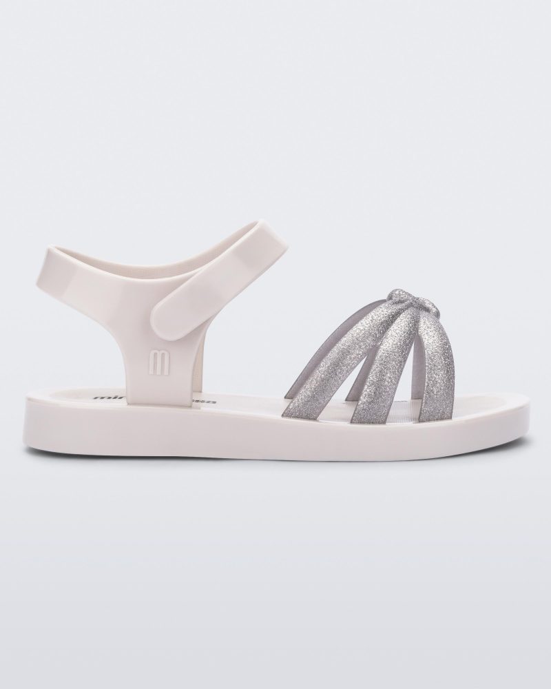 Side view of a white/silver Mini Melissa Precious sandal with three silver glitter front straps joining in the middle and a white ankle strap.