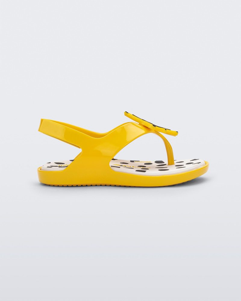 Side view of a yellow Mini Melissa Sunny sandal with a black base, a banana drawing on top of the straps and a black and white polka dot insole.