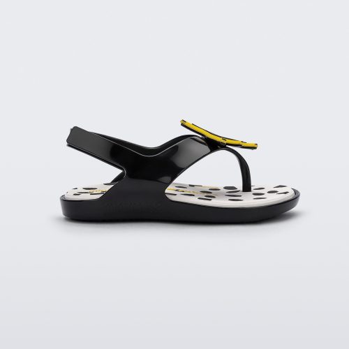 Side view of a black Mini Melissa Sunny sandal with a black base, a banana drawing on top of the straps and a black and white polka dot insole.