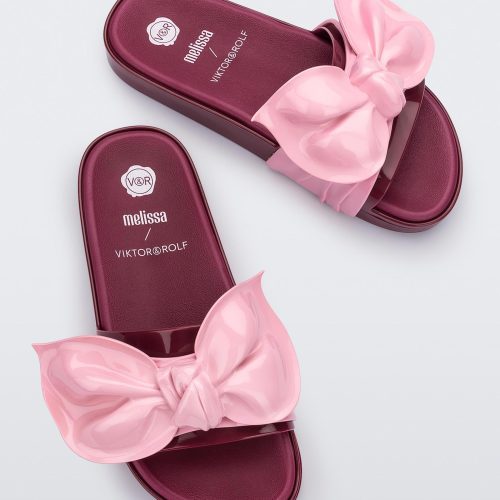 A top view of a pair of red/pink Melissa Tie Beach slides with a red base and a pink bow on the front strap.