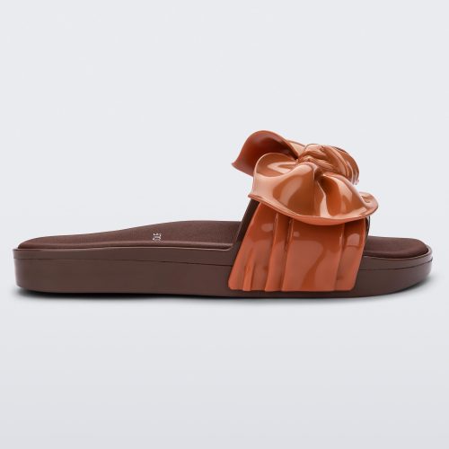 Side view of a Melissa Tie Beach slide with brown sole and brown/orange strap with 3D bow detail. 