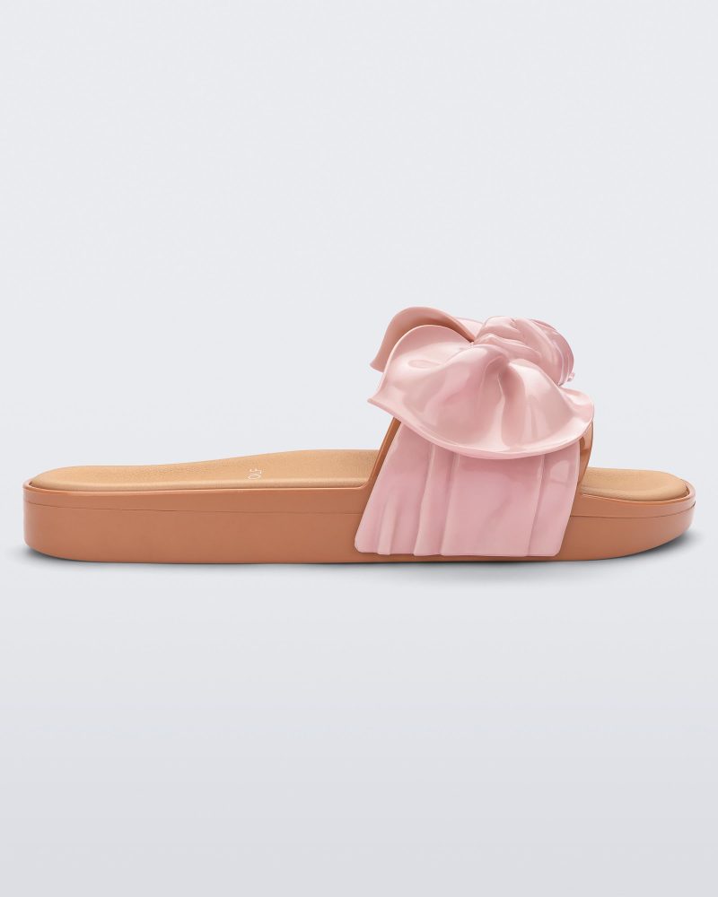 Side view of a beige/pink Melissa Tie Beach slide with a beige base and a pink bow on the top strap.