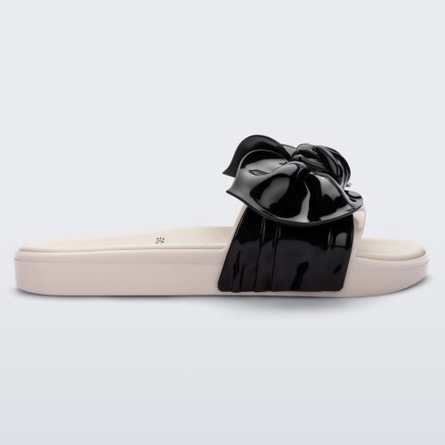 Side view of a Melissa Tie Beach slide with beige sole and beige/black strap with black 3D bow attached. 