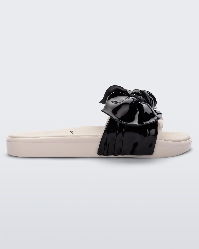 Side view of a Melissa Tie Beach slide with beige sole and beige/black strap with black 3D bow attached.