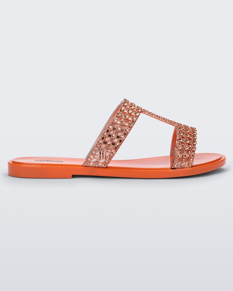 Side view of an orange / copper Melissa Glowing slide with copper gem stones on the straps and an orange sole.