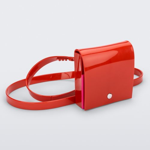 An angled front view of a red Melissa Like It purse with a silver button and a Melissa logo on the front.