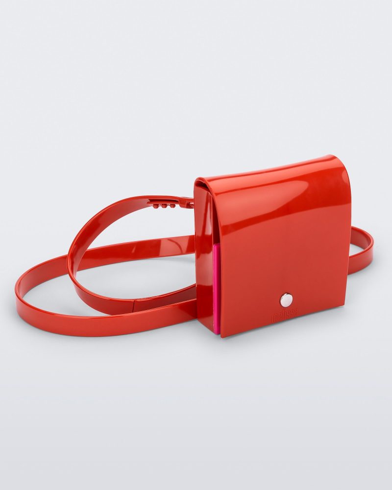 An angled front view of a red Melissa Like It purse with a silver button and a Melissa logo on the front.