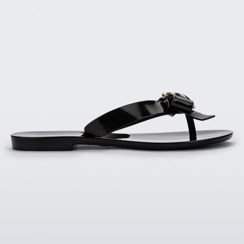 Side view of a black Melissa Harmonic Heart flip flop with a black bow and gold heart detail on the straps