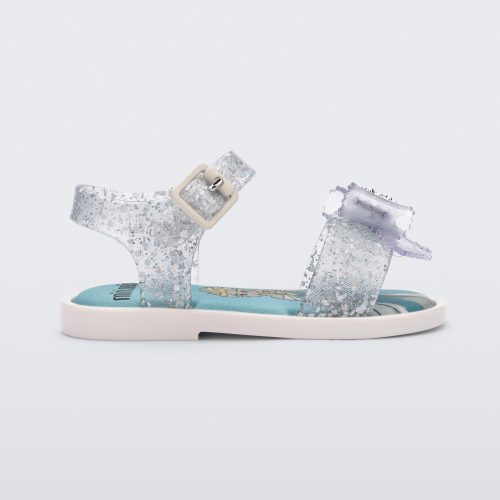 Side view of a glitter clear Mini Melissa Mar Sandal Princess sandal with a snowflake bow detail on the front strap, an ankle strap and Princess Elsa soul