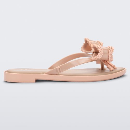 Side view of a beige Melissa Slim flip flop with a lace like bow detail on the front strap.