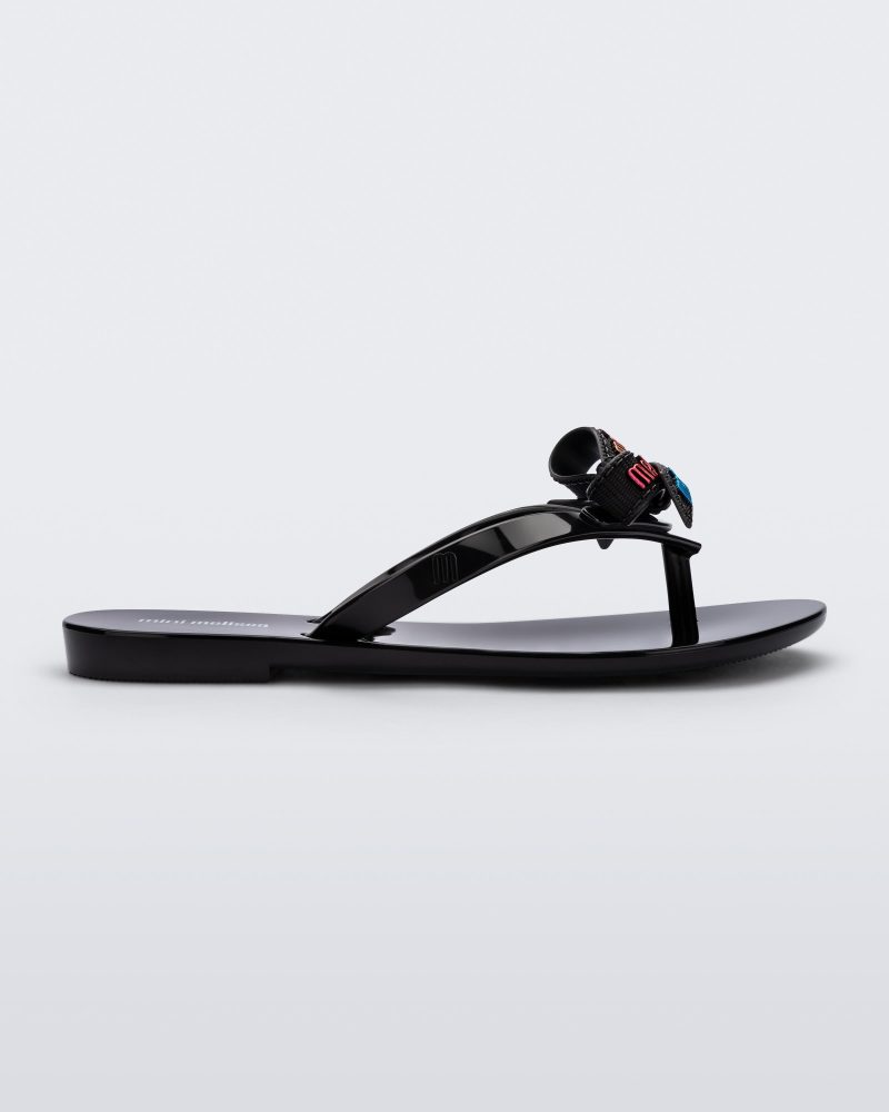 Side view of a black Harmonic M Lover kids flip flop with rainbow Melissa logo on bow