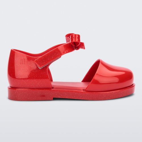 Side view of a red Mini Melissa Amy sandal with a red closed toe section and a back red glitter strap with a lace like bow detail.