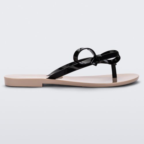 Side view of a beige/black Melissa Harmonic Sweet flip flop with a beige sole and black straps with a bow detail on the front.