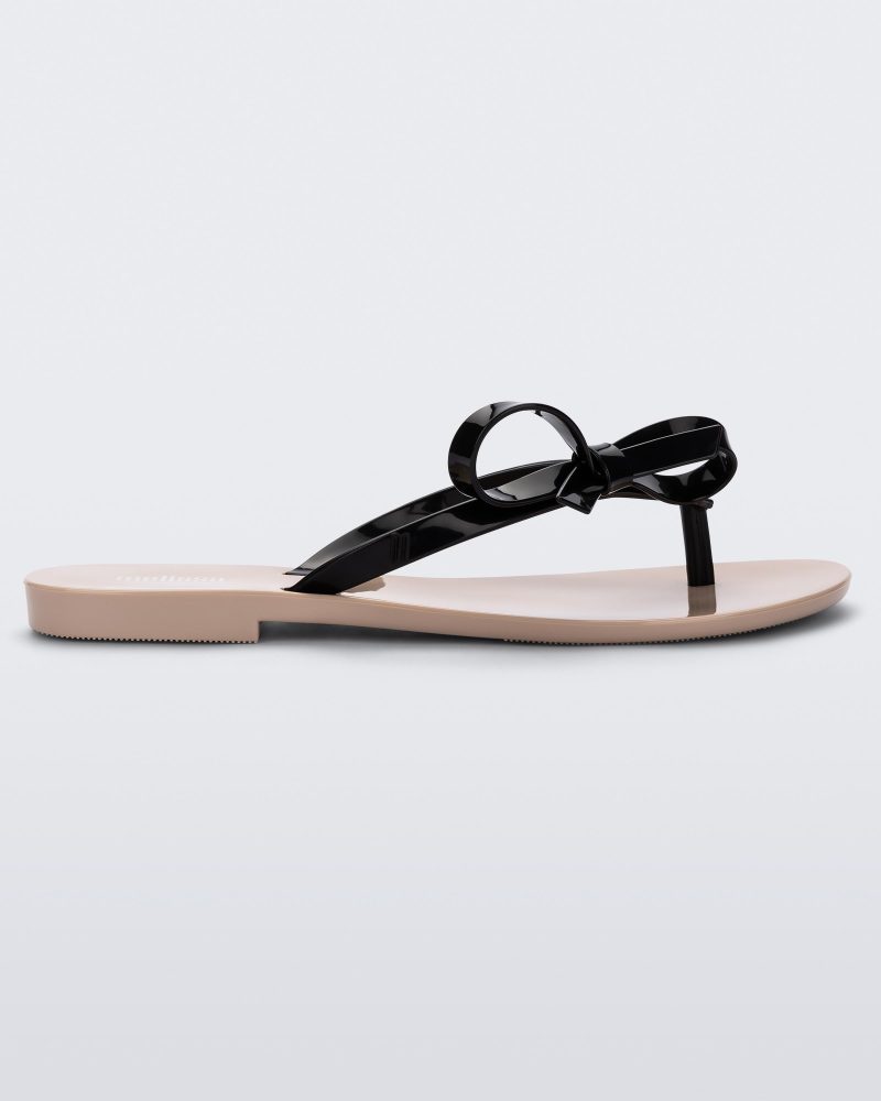 Side view of a beige/black Melissa Harmonic Sweet flip flop with a beige sole and black straps with a bow detail on the front.