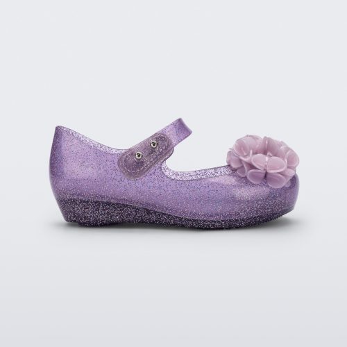 Side view of a clear purple glitter Ultragirl Springtime baby flat with two purple flowers and peep toe.