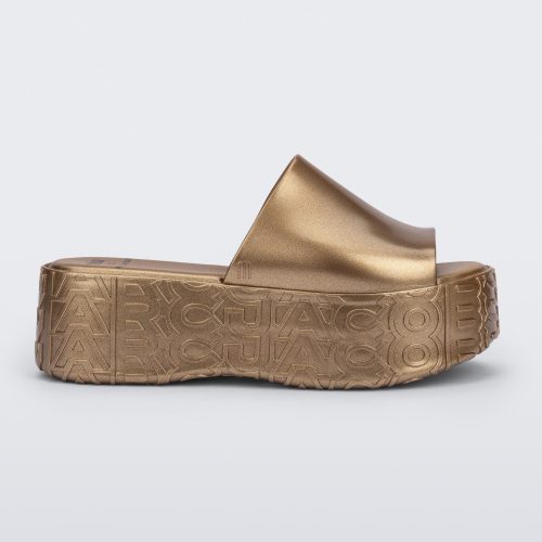 Side view of a gold Becky + Marc Jacobs platform slide.