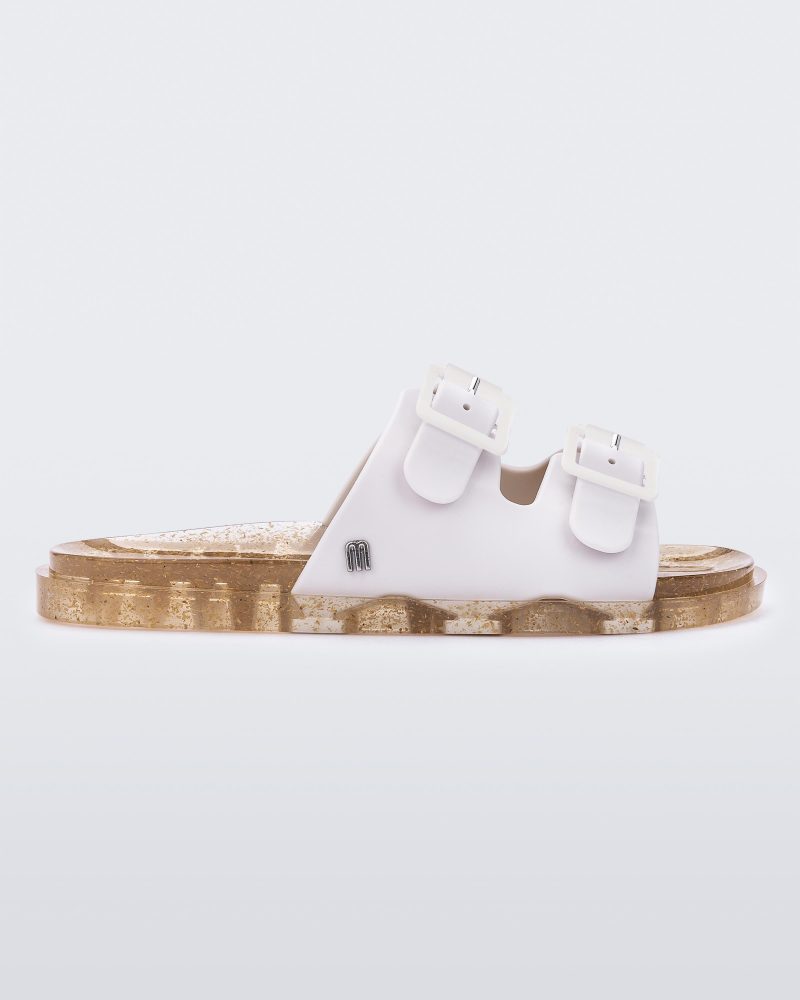 An outter side view of a Beige Mini Melissa Wide Slide with a white top with two white buckles and a beige sole.