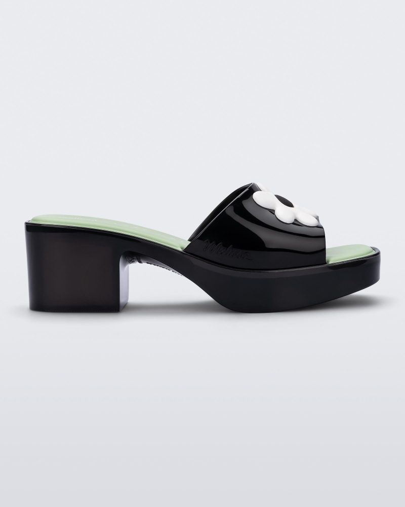 Side view of a Melissa Shape slide sandal in black with platform heel, black front strap with white flower detail and a green insole.