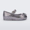 An outter side view of a silver glitter Mini Melissa Sweet Love flat with a top strap and a bow detail on the toe.