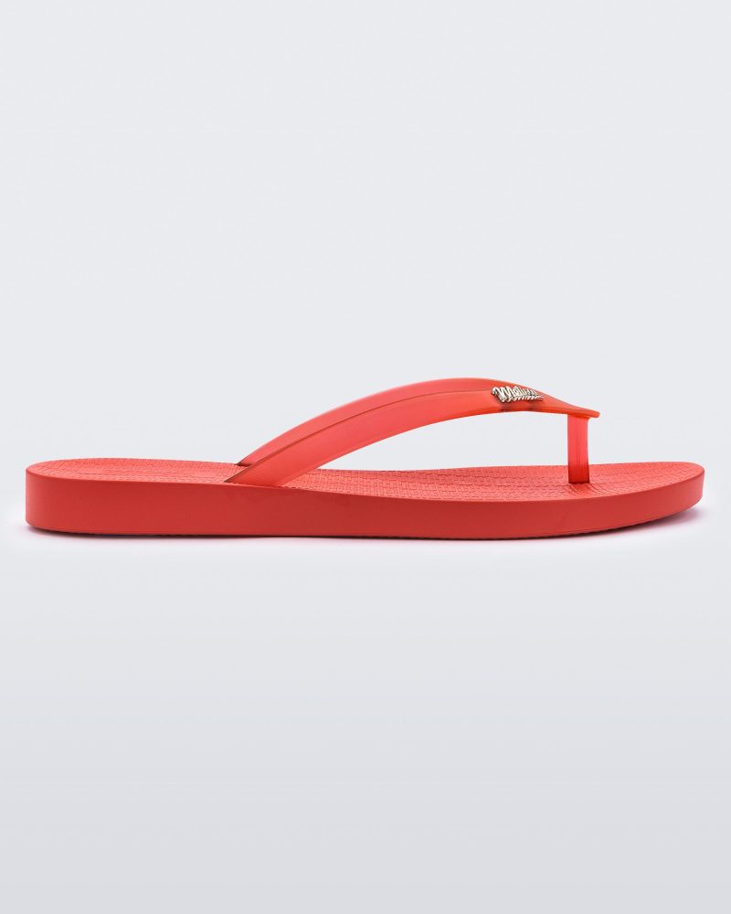 An outter side view of a red Melissa Sun Venice flip flop with a "melissa" logo on the strap.