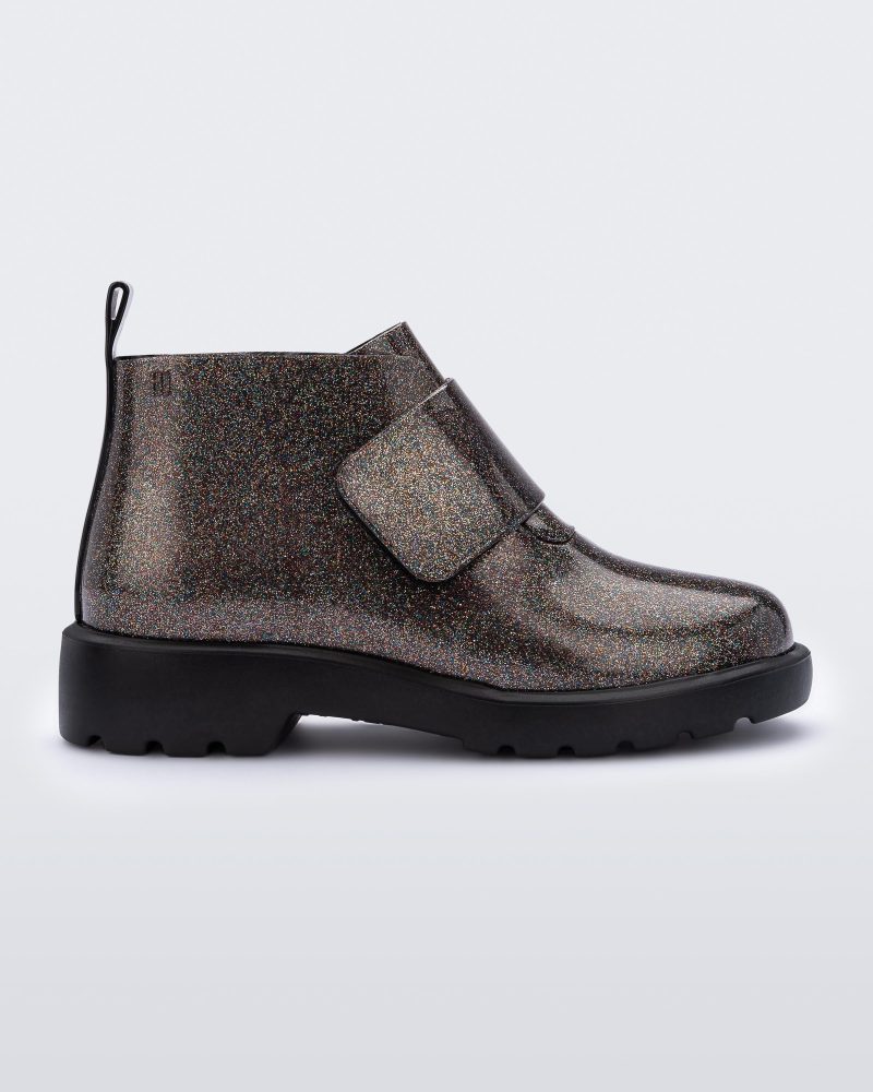 An outter side view of a black/glitter multicolor Mini Melissa Chelsea boot with a glitter multicolor base, velcro front strap and black sole.