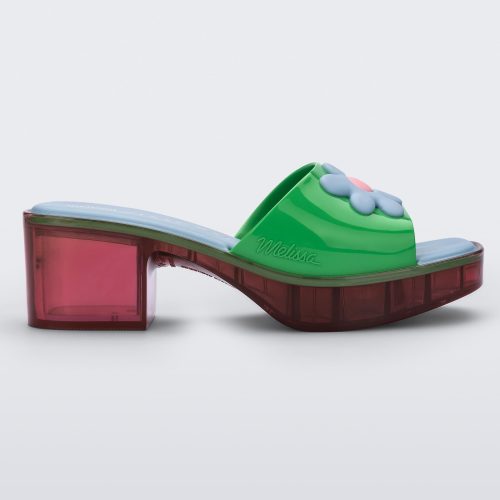 Side view of a multicolored Melissa Shape heeled slide, with transparent pink sole and green strap with blue and pink flower in the center.